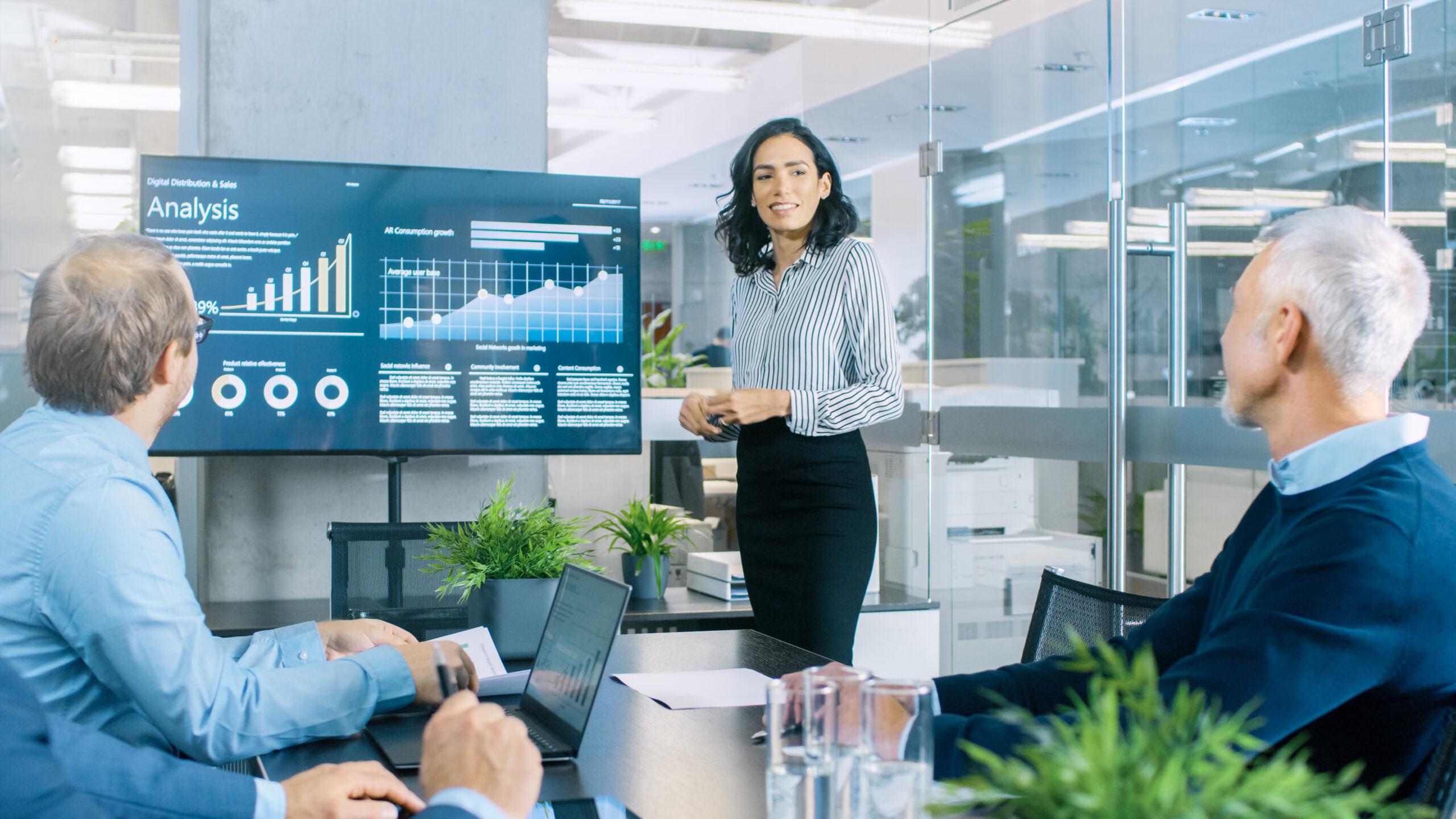 Female Executive Gives a Report/ Presentation to Her Colleagues in the Meeting Room, She Shows Graphics, Pie Charts and Company's Growth on the Wall TV. Vice President