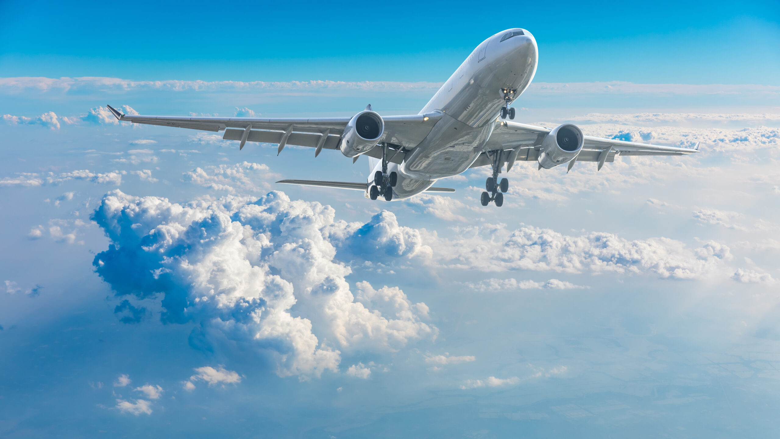 Commercial airplane flying above blue sky and white clouds.