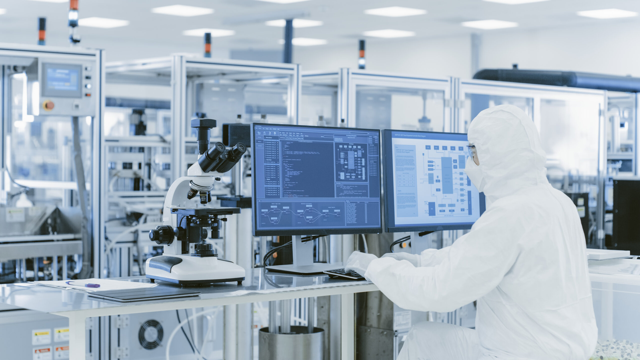 In Laboratory Over the Shoulder View of Scientist in Protective Clothes Doing Research on a Personal Computer. Modern Manufactory Producing Semiconductors and Pharmaceutical Items.