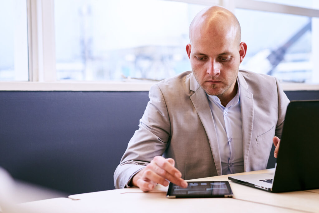 Bald, white business man working hard on his notebook and tablet early in the morning in the board room, concentrating and deep in thought while being productive.